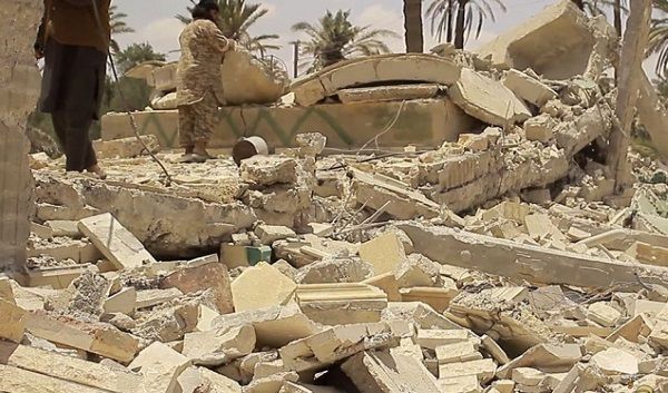 Imagen enviada por los militantes del EI que ya ha sido verificada, en donde se muestran a dos militantes sobre las ruinas de uno de los mausoleos destruidos.
