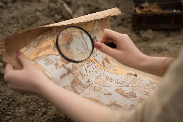 Persona arqueóloga con una lupa investigando un papiro antiguo