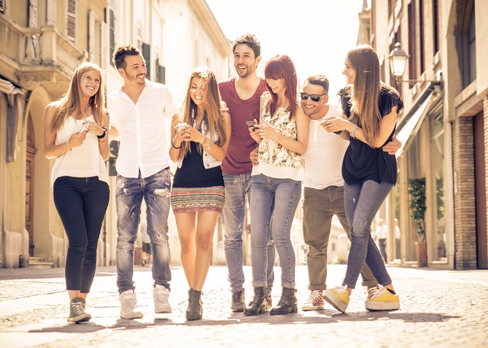 Grupo de amigos de pie en la calle sonriendo y con los móviles. Sodexo Pluxee