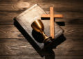 Biblia, cruz de madera y cáliz dorado sobre tela oscura, símbolos fundamentales de la religión cristiana y su historia de dos mil años