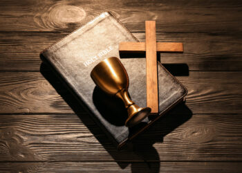 Biblia, cruz de madera y cáliz dorado sobre tela oscura, símbolos fundamentales de la religión cristiana y su historia de dos mil años