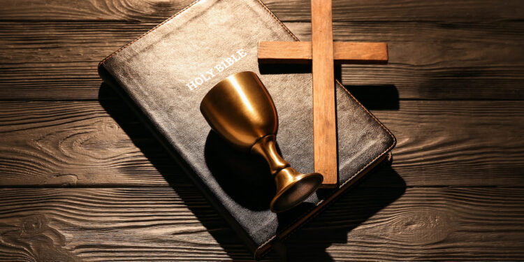 Biblia, cruz de madera y cáliz dorado sobre tela oscura, símbolos fundamentales de la religión cristiana y su historia de dos mil años