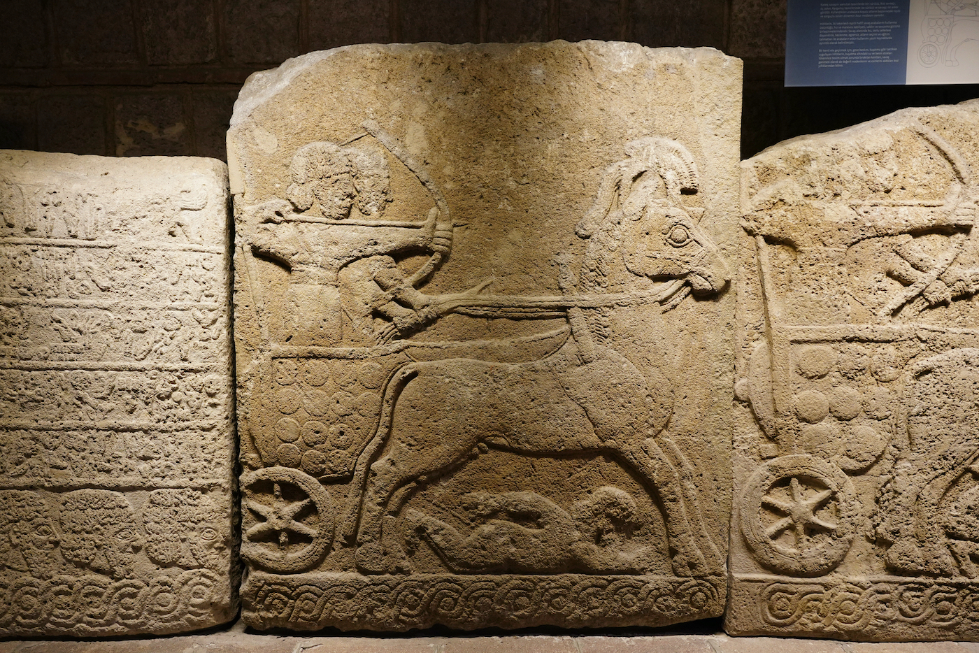 Relieve de piedra que muestra carro de guerra hitita con arquero y conductor, arte ceremonial de Hattusa.