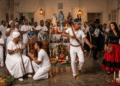 Ceremonia de umbanda con un preto velho sentado con bastón, un caboclo con arco y tocado de plumas y una pombagira con vestido rojo y negro, ante un altar sincrético con santos católicos y ofrendas