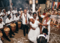 Ceremonia de vudú haitiano en un peristilo con houngan portando ason, mambo asistiendo a una iniciada en trance, tambores sagrados, altar sincrético y vévés de Legba y Baron Samedi trazados en el suelo